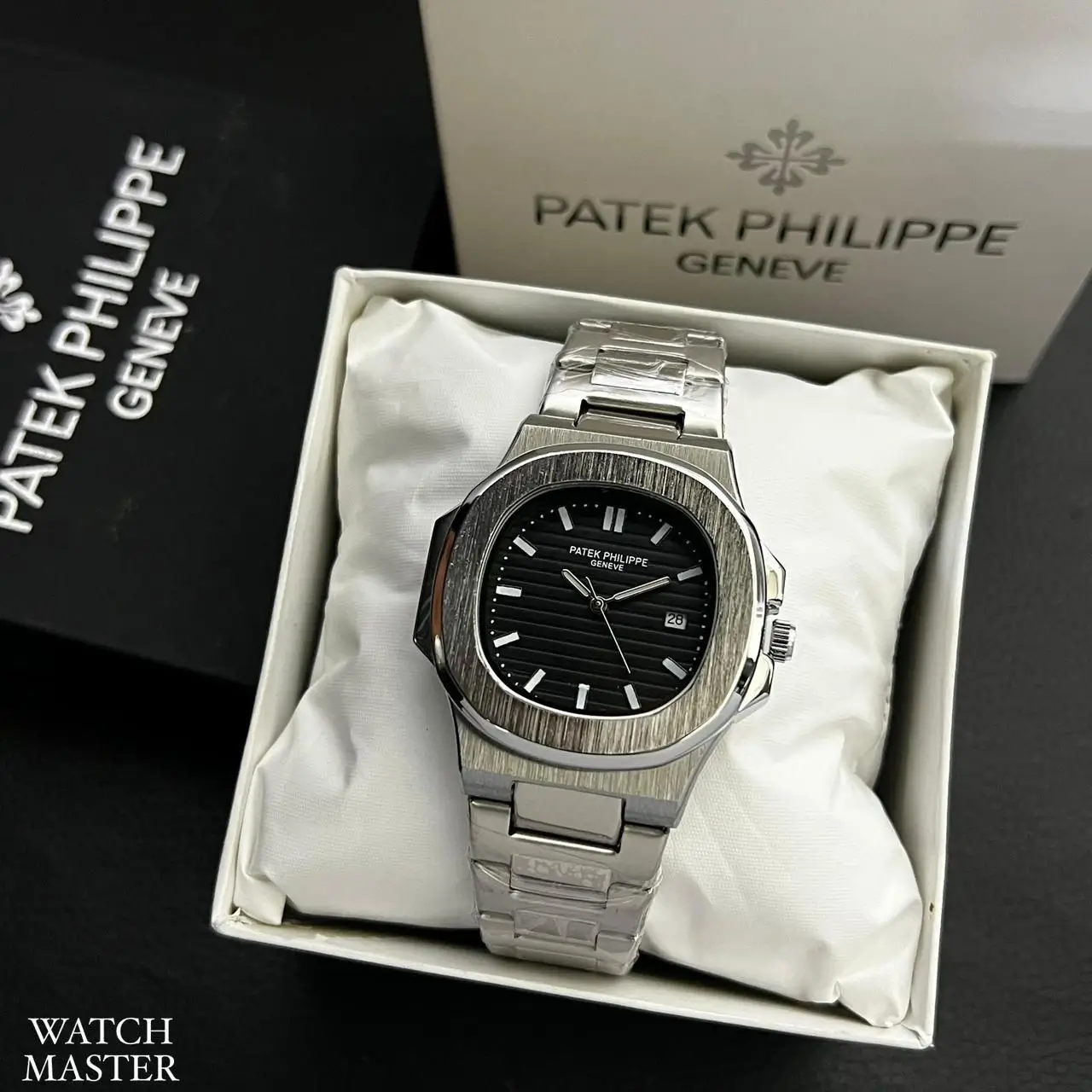 Luxury silver wristwatch with a black dial and date display placed in a white gift box, branded with Patek Philippe Genève packaging in the background