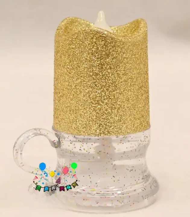 Glitter party mug candle with gold top, clear mug base, and festive birthday balloon graphics